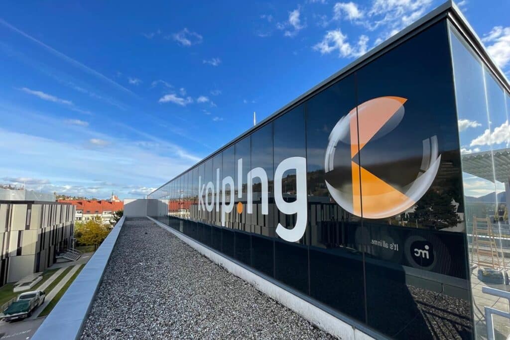 Beschriftung einer Glasfassade mit Selbstklebefolienbuchstaben und Klebelogo, 2m Höhe mal 8,5m Länge, gesicherte Montage am Dachgeschoss im 4. Stock